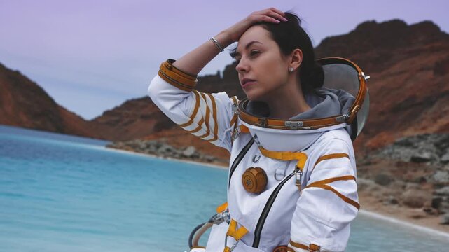 Serious woman astronaut looking at camera while sitting on a rock by an alien lake