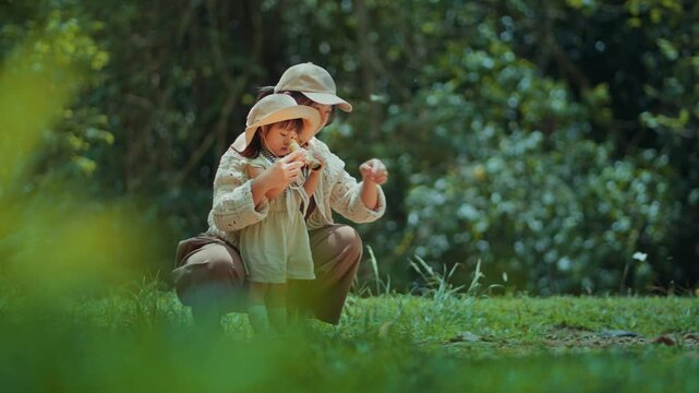 Asian mother teaching toddler daughter to use binoculars while watching butterflies in nature, outdoor learning and family exploration