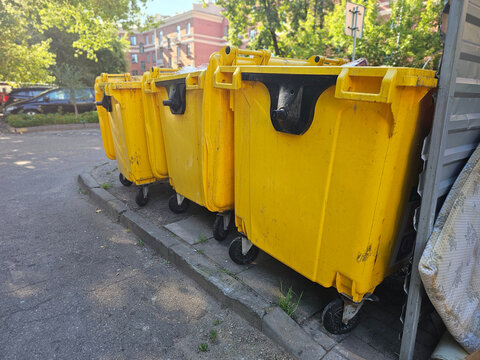 Four yellow trash bins lined up on a street outside