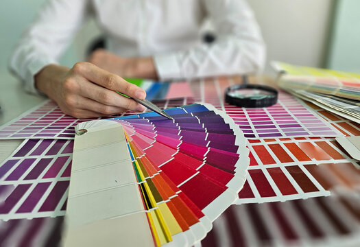 Color matching process with color swatches and a hand holding a paintbrush in a workspace