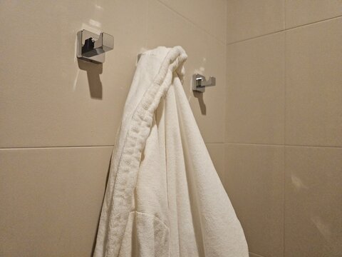 White bathrobe hanging on hooks in a tiled bathroom