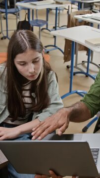 Vertical shot of Middle Eastern male teacher explaining lesson on laptop to Caucasian teenage girl student in classroom. Clip is ideal for promoting school curriculum and e-learning platforms