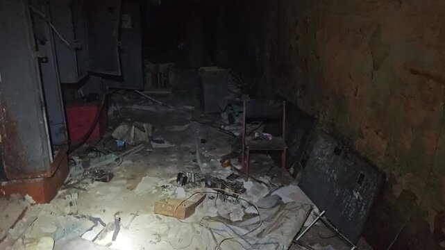 POV walking with a flashlight through a dark, ruined abandoned industrial corridor with electronic debris and broken cabinets.