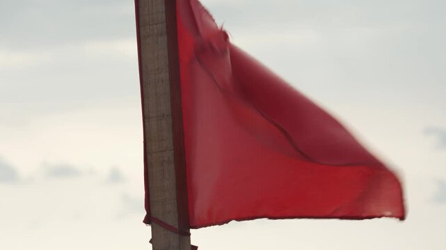 Red warning flag waving on a wooden pole against a cloudy sky, signaling dangerous conditions
