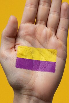 Close up of human hand holding intersex pride flag painted on palm. Yellow, violet stripes symbolise gender identity, diversity. Person shows support for intersex rights, visibility against