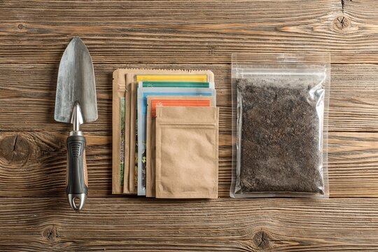 Garden trowel alongside paper seed packets and soil bag on aged wooden table surface