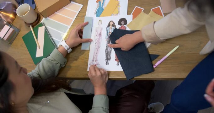 Diverse female colleagues reviewing sketches at table placing dark denim swatch checking tone