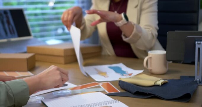 African woman in blazer checking sketches and swatches for review after hands passing sheet at desk