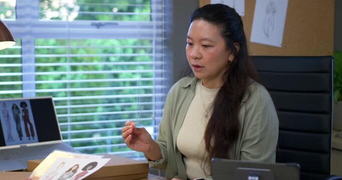 Asian woman sitting at desk in studio with laptop, responding to swatch while evaluating samples