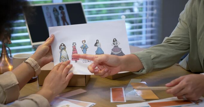 Diverse female designers sorting swatches, pointing at sketches, choosing fourth design at studio