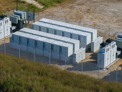 Aerial view of an electrical substation with rows of grey power storage cabinets and cooling units enclosed by a metal fence in the Netherlands.