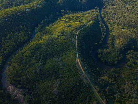 Aerial view of a winding river flowing through a dense forest with a dirt path cutting through the lush green landscape in Wonga Park, Victoria, Australia.