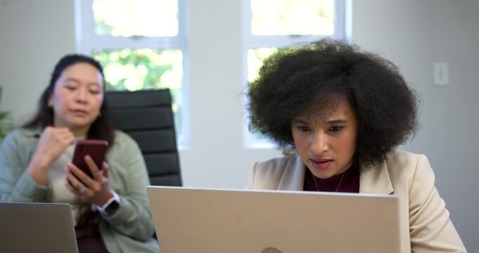 Diverse female team African American in blazer reacting to laptop as Chinese peer scrolling phone