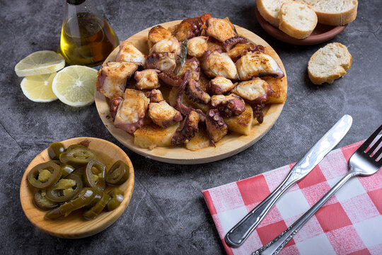 Traditional Spanish octopus tapa served on a wooden plate with potatoes, olive oil, lemon, bread, and spices on a dark background