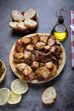 Traditional Spanish octopus tapa served on a wooden plate with potatoes, olive oil, lemon, bread, and spices on a dark background
