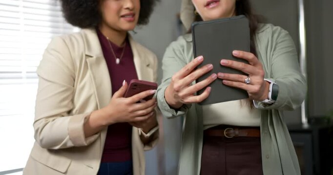 Diverse female pair in blazers right woman showing tablet left woman pointing swiping phone at work