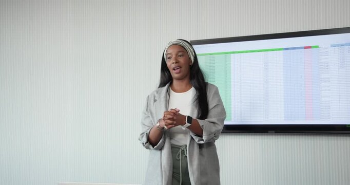Woman starting talk, pointing at spreadsheet on display while holding tablet in conference room