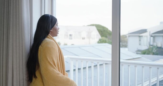 Balcony door drawing African American woman wrapping shawl for warmth, looking at roofs, copy space