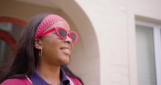 African American woman facing sun on porch smiling adjusting red cateye shades peeking putting them
