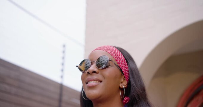 African American woman noticing sky, raising hands and adjusting round sunglasses at home, smiling
