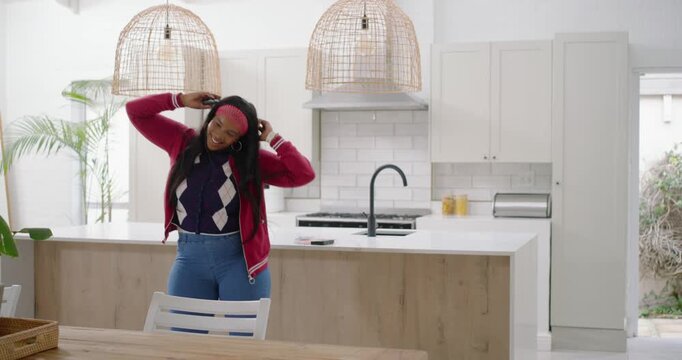 African American woman entering kitchen, smiling at phone and dancing while adjusting pink headband