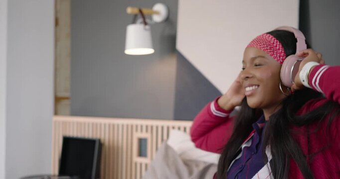 African American woman hearing vinyl, putting pink headphones on, nodding on bed, copy space