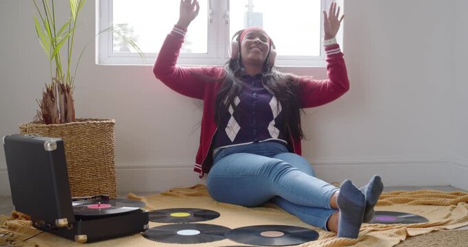 Turntable starting music, African American woman adjusting headphones at home raising arms