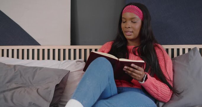 Camera zoom showing African American woman sitting on bed, reading journal, smiling in reflection