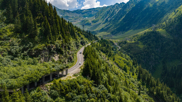 Aerial view of the Transfagarasan mountain road winding through lush green forests and steep slopes in the Carpathian Mountains, Curtea de Arges, Judetul Arges, Romania.