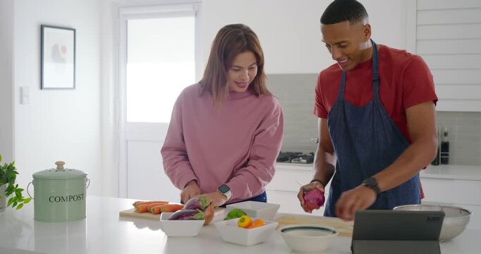 Diverse couple following tablet recipe, chopping vegetables, passing produce and arranging bowls