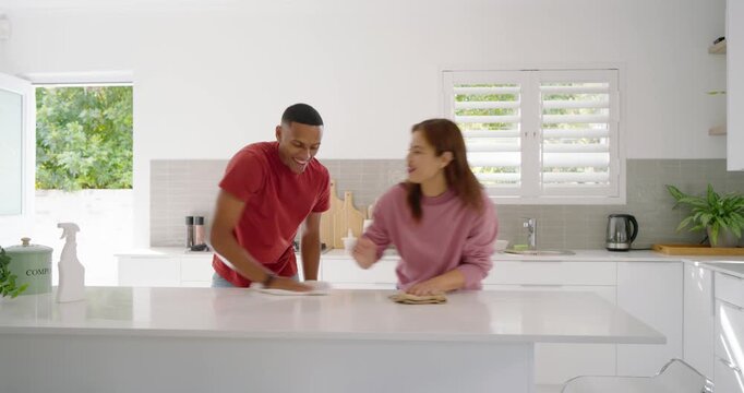 Couple cleaning white island in kitchen, cloths in hands, teasing with spray bottle and laughing