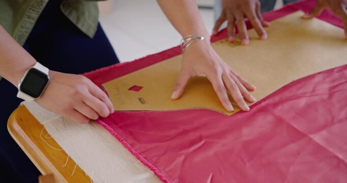 African American couple at table placing pattern, smoothing red cloth, tracing, cutting to sew