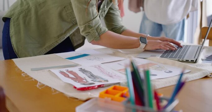 African American designers leaning, sorting sketches and checking designs on laptop in studio