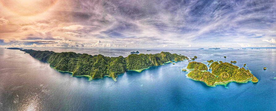 Aerial view of Raja Ampat Regency featuring lush green islands surrounded by turquoise waters and coral reefs under a dramatic sky in Southwest Papua, Indonesia.