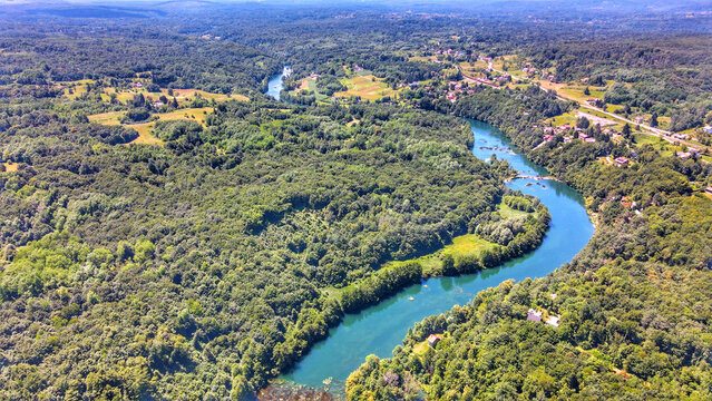 Aerial view of the winding Mreznica river flowing through lush green forests and rural landscapes in Mreznica, Karlovac County, Croatia.