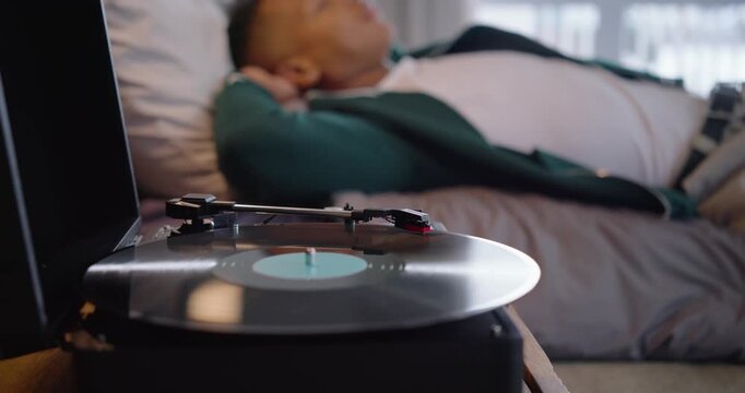 Spinning vinyl on player drawing camera toward African American man reclining in bedroom listening