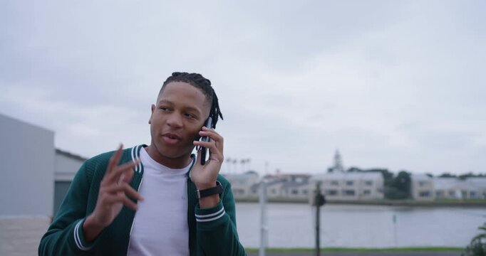 African American adult man answering phone explaining plans leaning on railing by water in jacket