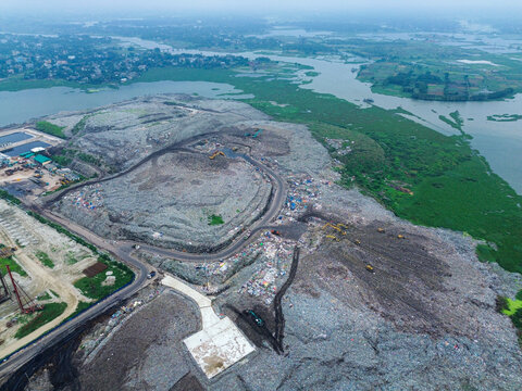 Aerial view of Amin Bazar Waste Disposal Area showing large piles of waste, heavy machinery, and surrounding wetlands in Bongaon Union, Dhaka Division, Bangladesh.