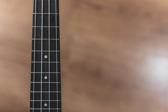 Ukulele neck with dark fretboard appears in close view. Metal frets form a clear pattern. White dot markers indicate positions. 