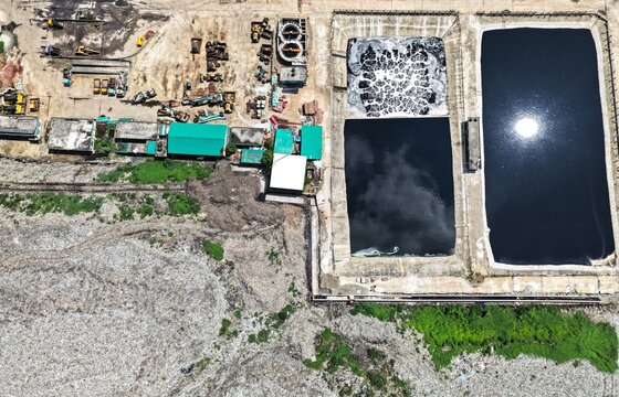 Aerial view of the Aminbazar Landfill showing waste management facilities, large dark treatment ponds, and heavy machinery in Aminbazar, Dhaka Division, Bangladesh.