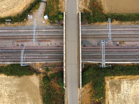 Aerial view of a bridge crossing over railway tracks surrounded by rural fields and vegetation in Finedon, England, United Kingdom.