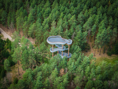 Aerial view of the modern observation tower rising above the dense pine forest canopy in Merkine, Alytus County, Lithuania.