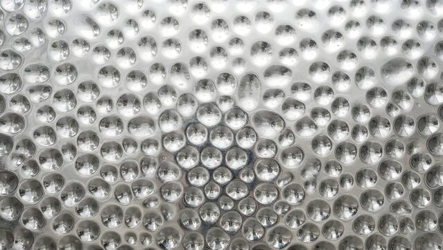 Close-up abstract background of a textured metallic surface with a pattern of raised circular bumps reflecting light.