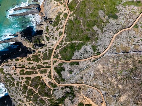 Aerial view of the wooden boardwalks winding through the Parque ecologico da Adraga, featuring rugged coastal cliffs and the Atlantic Ocean in Colares, Lisboa, Portugal.