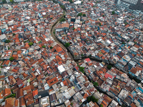 Aerial view of dense urban housing with terracotta rooftops and a narrow river flowing through the neighborhood in Bandung, West Java, Indonesia.