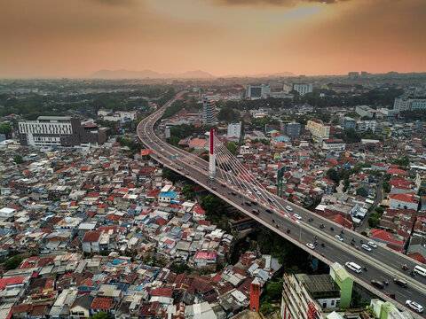 Aerial view of the Pasupati Bridge spanning over the dense urban landscape with rooftops and golden hour light in Bandung, West Java, Indonesia.