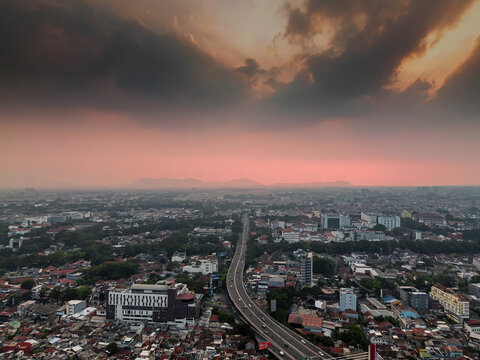 Aerial view of Jembatan Pasteur - Surapati highway winding through the urban landscape of Bandung at sunset with dramatic clouds and city buildings. Bandung, West Java, Indonesia.