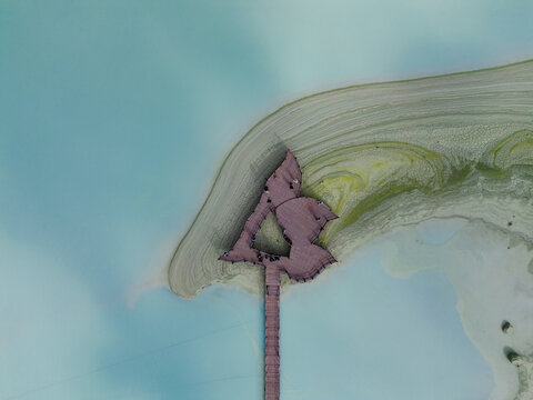 Aerial view of Kawah Putih Ciwidey featuring a wooden pier extending into the turquoise volcanic lake with unique shoreline patterns in Bandung, West Java, Indonesia.