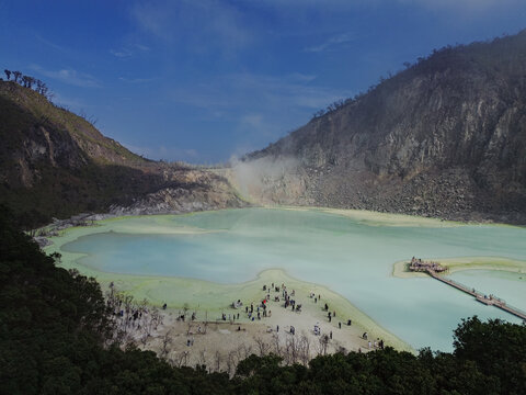 Aerial view of Kawah Putih Ciwidey crater lake with its turquoise water, sulfurous steam, rocky walls, and tourists on the shore in Bandung, West Java, Indonesia.