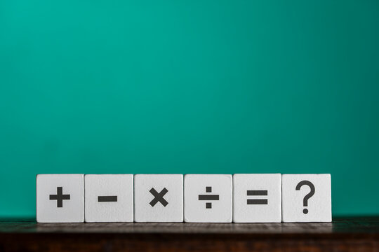 Math symbols and question mark on wooden blocks, closeup. Six white wooden cubes with printed mathematical symbols plus minus multiply divide equals and question mark on green background